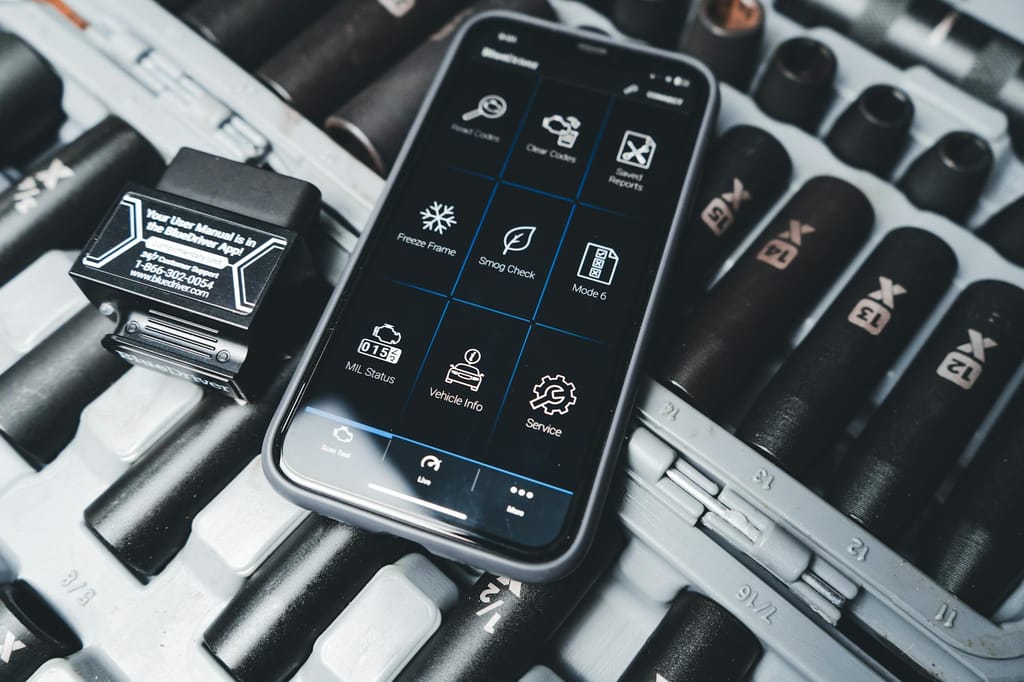 Close-up of a smartphone showing car diagnostic app with OBD2 scanner in a garage setting
