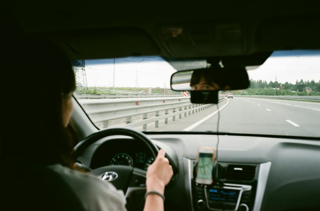 A woman driving a car on the highway, using GPS navigation on her smartphone.
